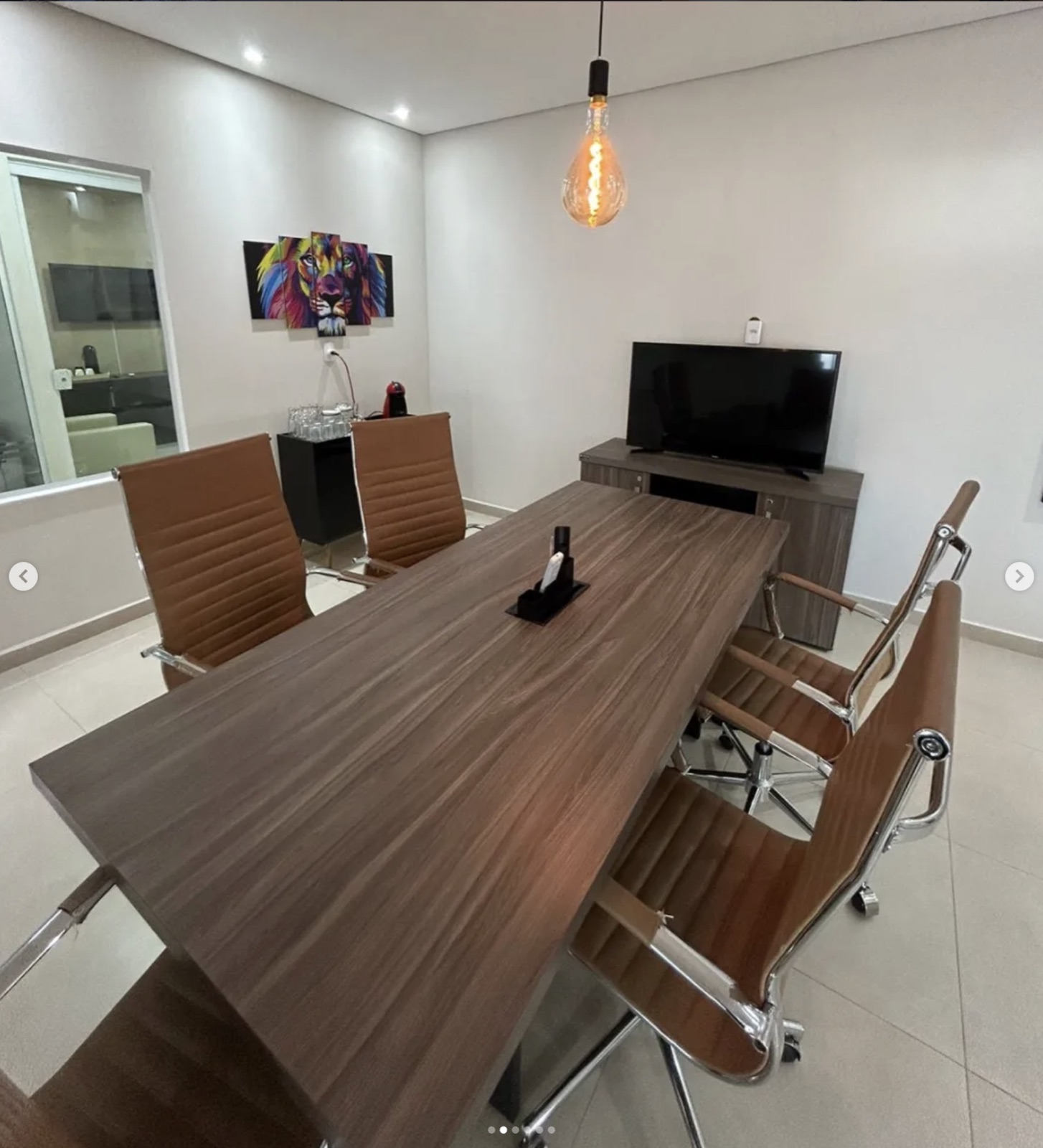 Sala de reunião com mesa, cadeiras, TV e café